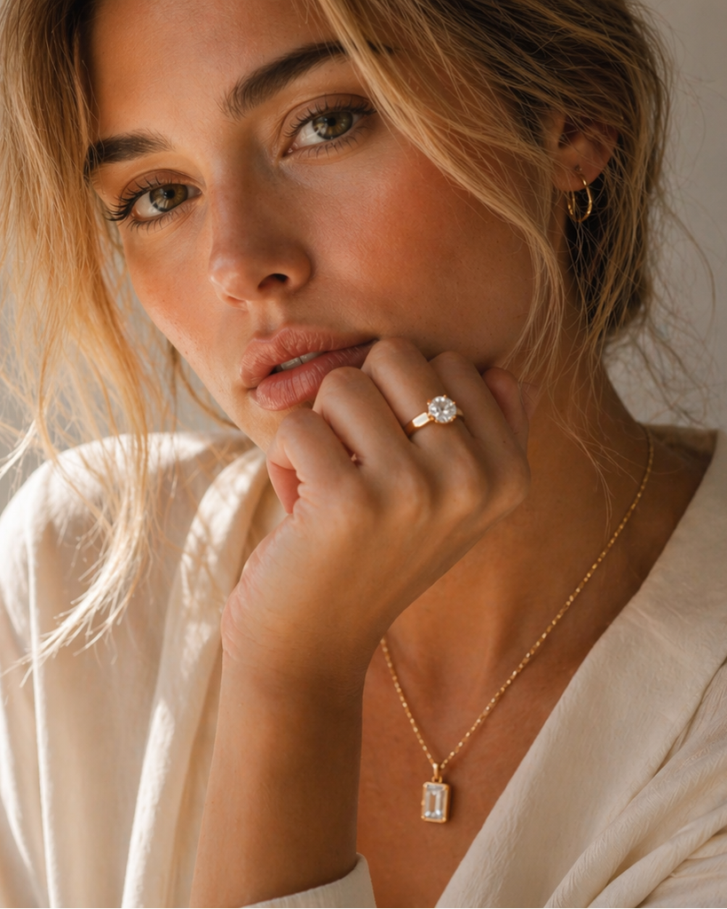 Woman wearing a ring and necklace against a neutral background